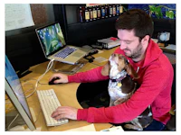 a man sitting at a desk with a dog on his lap